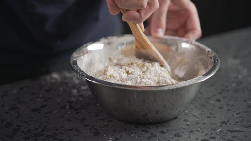 Man Mixing Wet Ingredients Into Flour In Steel Bowl On Concrete