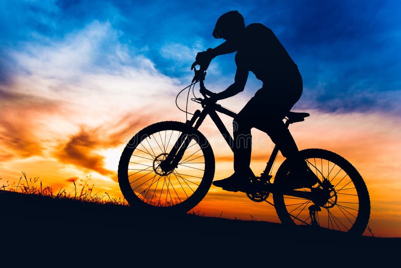 Man on mountain bike at sunset, riding bicycle on hills