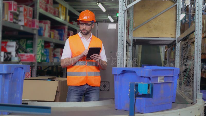 Warehouse worker standing near conveyor with parcels. Manager using digital tablet entering data. Man controls logistic wearing uniform and white shirt. Controls automation stock images, royalty-free photos and pictures