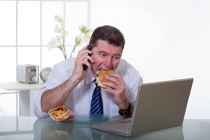 L'uomo in ufficio con telefono di mangiare cibo malsano.