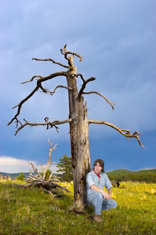 An outdoors enthusiast sits outside and looks into the distance as he enjoys the quiet and peace of a mountain meadow. The man has long brown hair. Adventurer adventure stock images, royalty-free photos and pictures