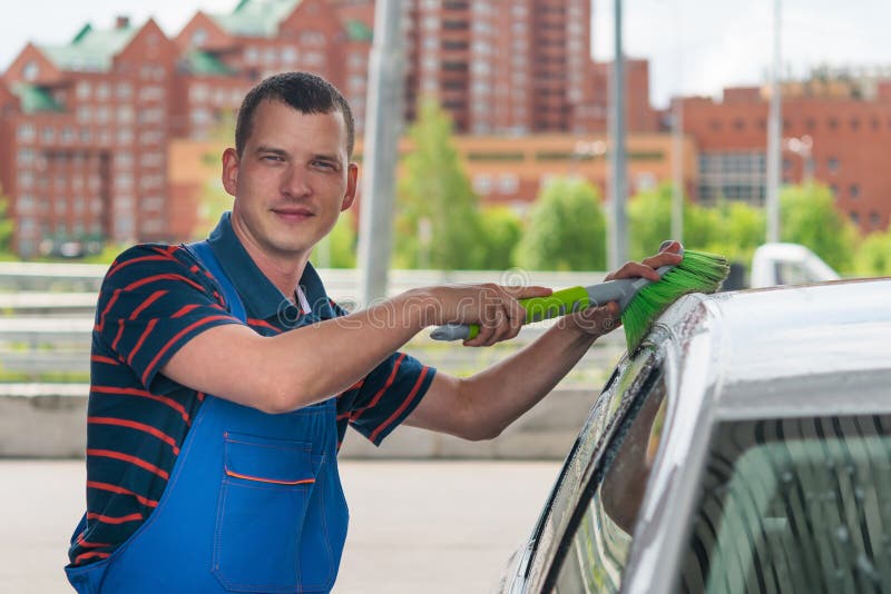 The man in the overalls washes the car with a brush on the car wash