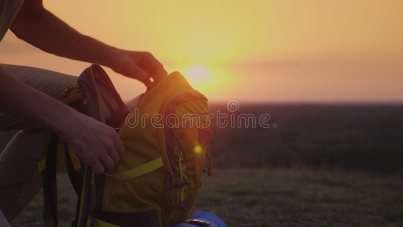 A man is packing his backpack at sunset. Preparing for a trip or trekking