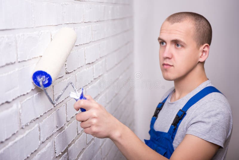 Man Painter in Workwear Painting Brick Wall with Paint Roller Stock