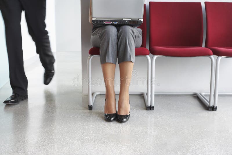 Man Pass By Woman With Laptop On Chair In Corridor