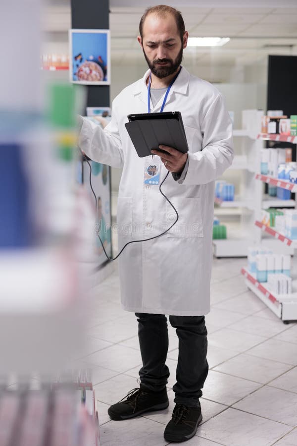 Man Pharmacist Looking at Medical Products Information on Tablet Computer while Scanning Drugs