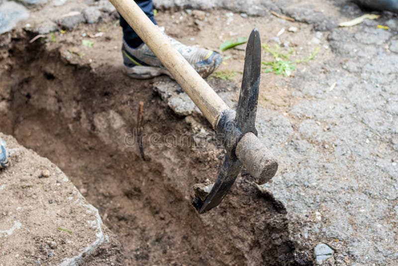 A man picks up hard ground with a pickaxe while digging a ditch on a construction site stock photos