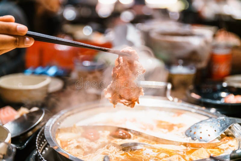 Man pinching boiled medium rare slice Wagyu A5 beef out from hot pot Mala soup base by chopsticks