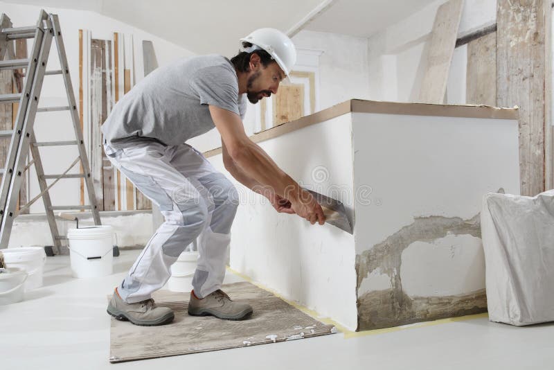 Man plasterer construction worker at work, takes plaster from bucket and puts it on trowel to plastering the wall, wears helmet