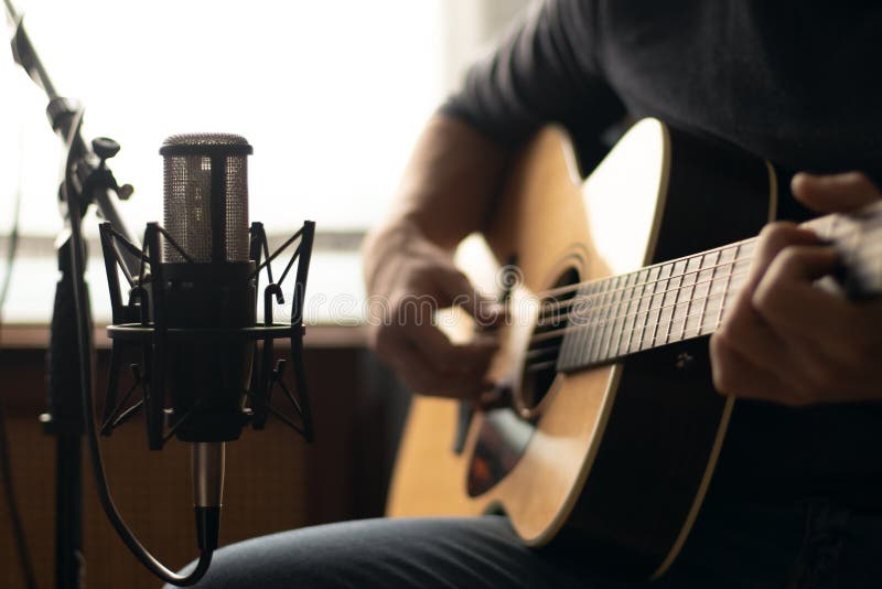 Man Playing Acoustic Guitar and Recording with a Microphone in a Room