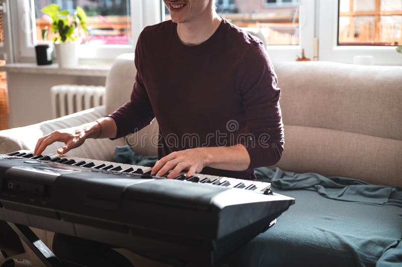 Man playing a digital keyboard in a relaxed home setting, seated on a sofa with natural light streaming in, capturing a peaceful and focused musical moment. Focused natural elegance stock images, royalty-free photos and pictures