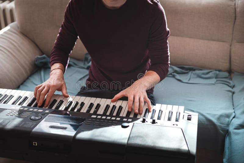 Man playing a digital keyboard in a relaxed home setting, seated on a sofa with natural light streaming in, capturing a peaceful and focused musical moment. Focused natural elegance stock images, royalty-free photos and pictures