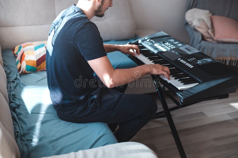 Man playing a digital keyboard in a relaxed home setting, seated on a sofa with natural light streaming in, capturing a peaceful and focused musical moment. Focused natural elegance stock images, royalty-free photos and pictures
