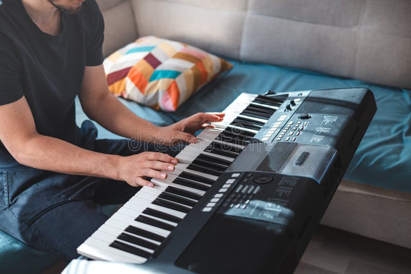 Man playing a digital keyboard in a relaxed home setting, seated on a sofa with natural light streaming in, capturing a peaceful and focused musical moment. Focused natural elegance stock images, royalty-free photos and pictures