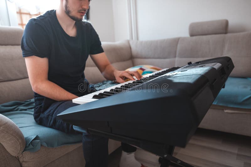Man playing a digital keyboard in a relaxed home setting, seated on a sofa with natural light streaming in, capturing a peaceful and focused musical moment. Focused natural elegance stock images, royalty-free photos and pictures