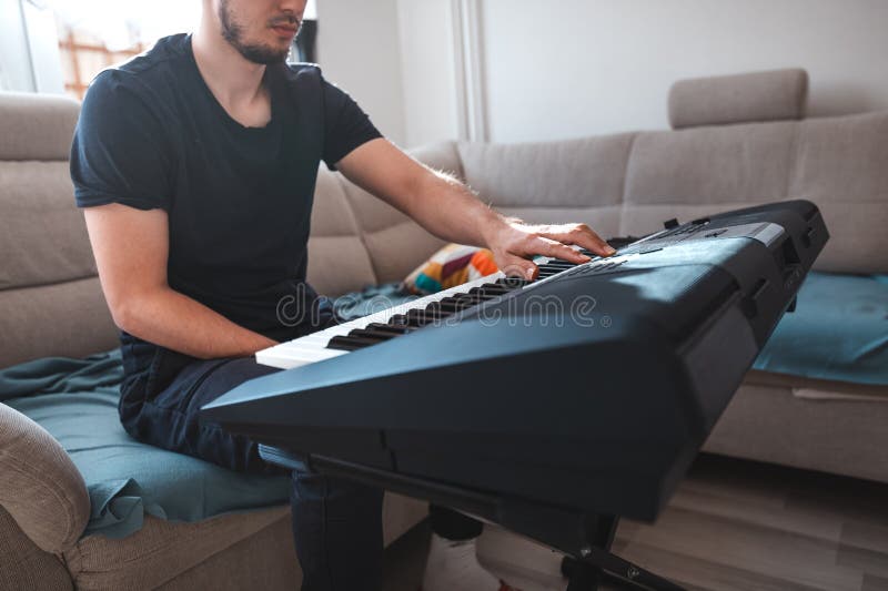 Man playing a digital keyboard in a relaxed home setting, seated on a sofa with natural light streaming in, capturing a peaceful and focused musical moment. Focused natural elegance stock images, royalty-free photos and pictures