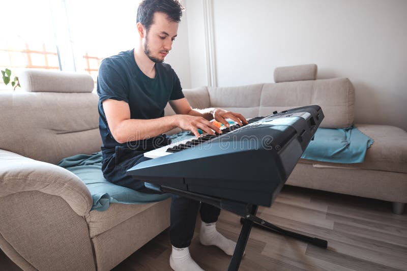 Man playing a digital keyboard in a relaxed home setting, seated on a sofa with natural light streaming in, capturing a peaceful and focused musical moment. Focused natural elegance stock images, royalty-free photos and pictures