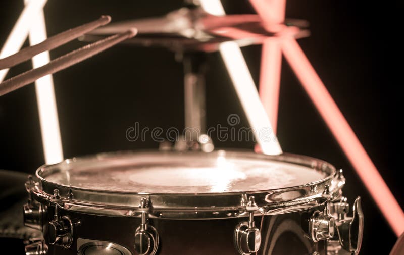 A man plays with sticks on a musical percussion instrument, close-up. On a blurred background of colored lights.