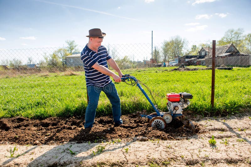 A Man Plows the Ground with a Tillerblock in the Garden Stock Photo