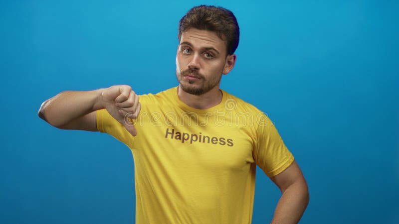 Man pointing index finger upward and showing thumbs down on yellow tshirt in blue studio; skepticism. Finger point down stock images, royalty-free photos and pictures