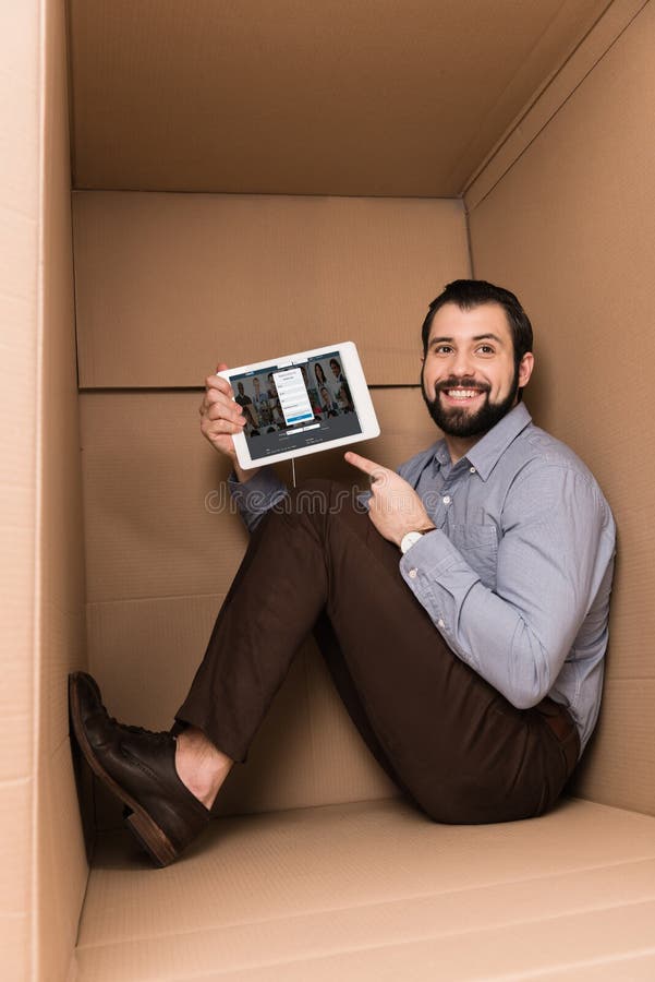 Cheerful handsome man pointing at tablet with linkedin website while sitting