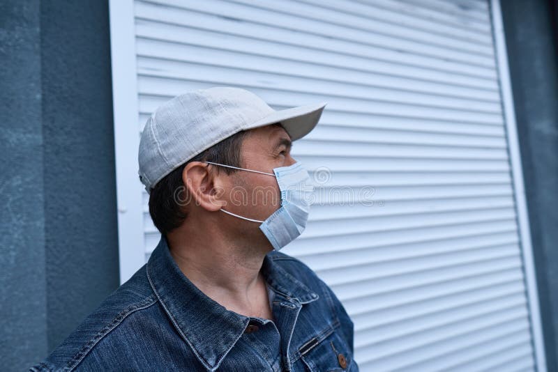 Man posing near wall and closed door of high-rise buildings with apartments, a residential area, a medical mask on his face stock image Man posing near wall and closed door of high-rise buildings with apartments, a residential area, a medical mask on his face stock image