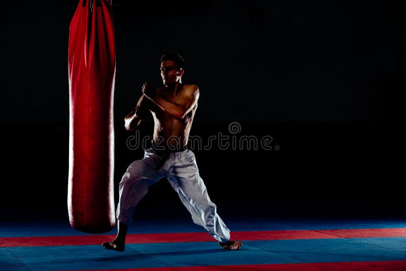 Man practicing boxing on big black bag in gym