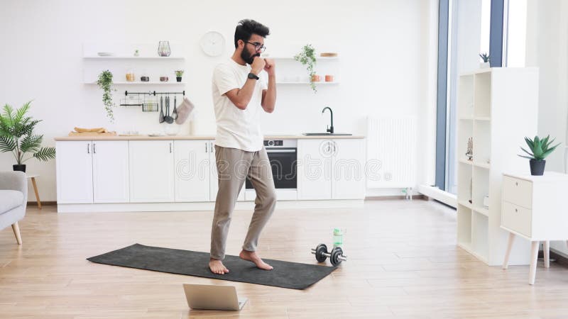 Man practicing boxing moves on yoga mat in modern kitchen interior space stock video