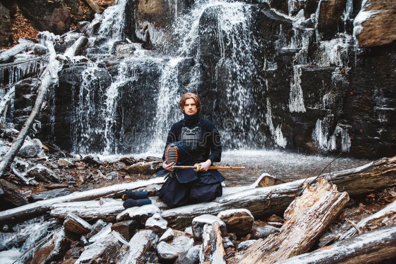 Man practicing kendo with bamboo sword on waterfall background. Place for text or advertising stock images