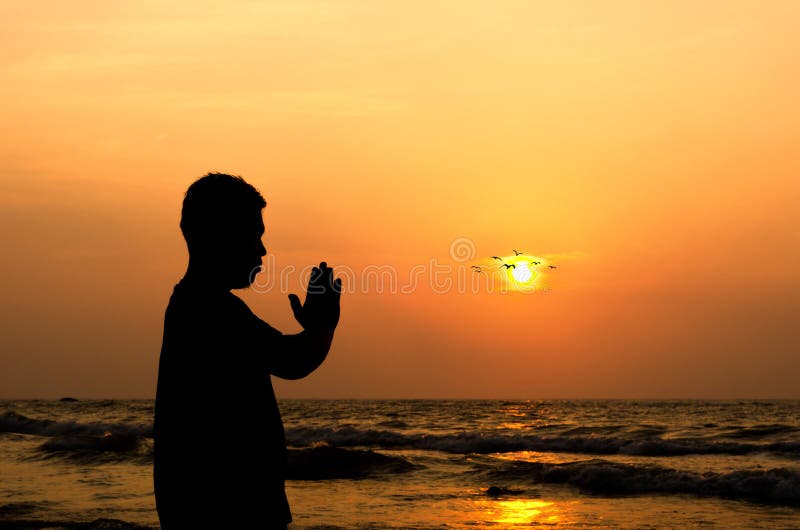A Man Praying in Front of a Golden Sunrise on the Beach Stock Image