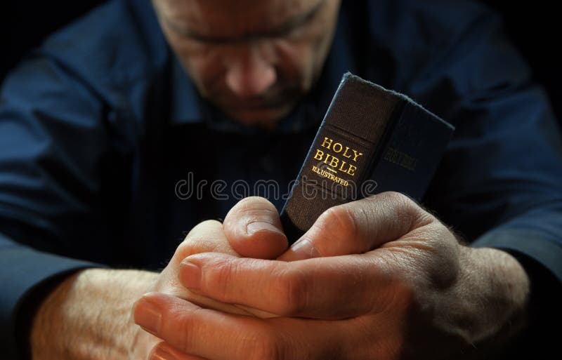 A Man praying holding a Bible.