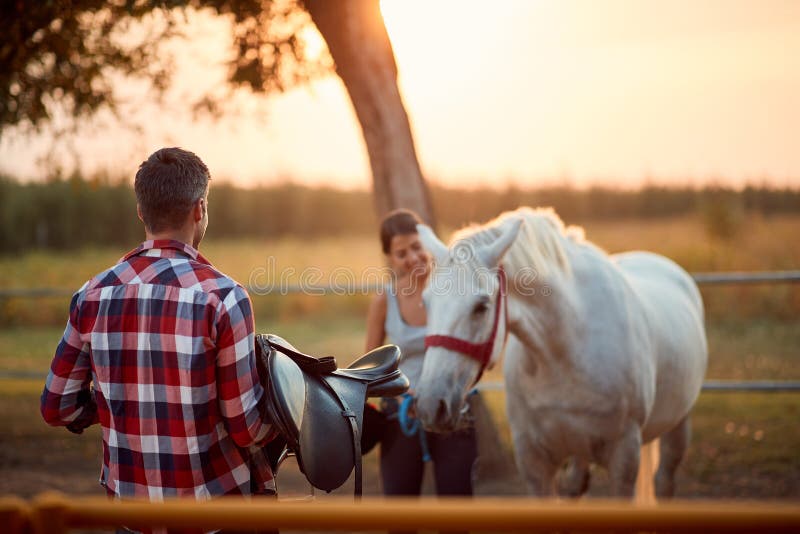 Man prepare saddle for horse. Couple enjoying on countryside at horse farm