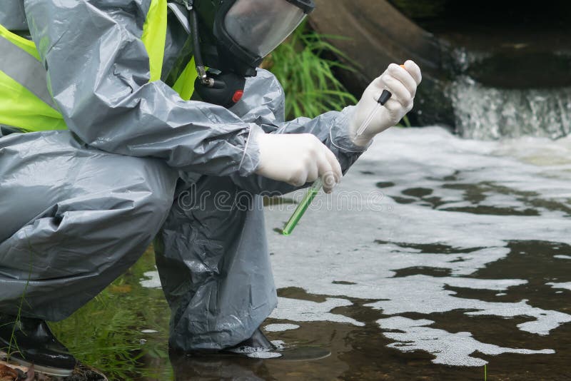 A man in a protective suit and mask holds a test tube and a pipette with test water on the river after an accident stock photography A man in a protective suit and mask holds a test tube and a pipette with test water on the river after an accident stock photography