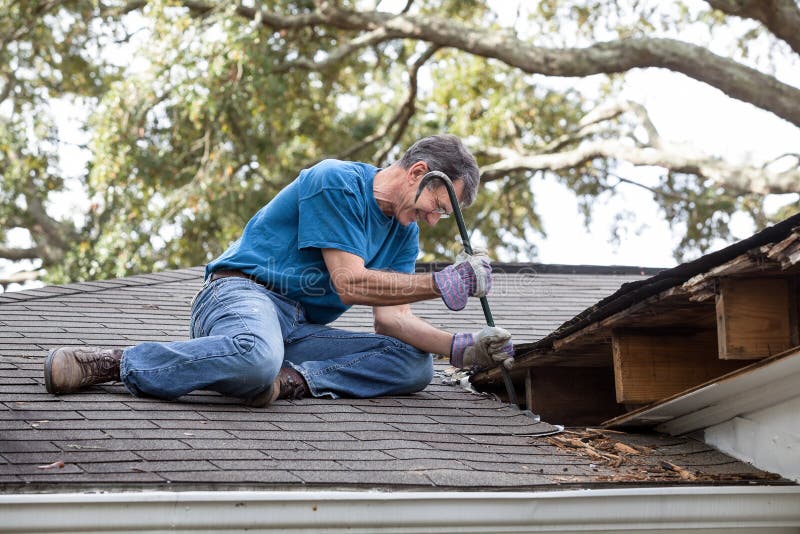 Man using crowbar to remove rotten wood from leaky roof. After removing fascia boards he has discovered that the leak has extended into the beams and decking. Man using crowbar to remove rotten wood from leaky roof. After removing fascia boards he has discovered that the leak has extended into the beams and decking.