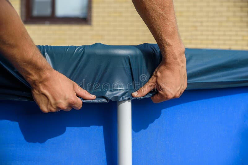 A man pulls up an cover over a home swimming pool.