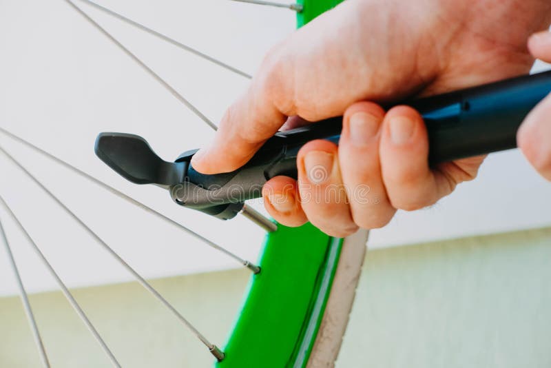 A Man Pumps Up a Green Bicycle Wheel with a Hand Pump Stock Photo