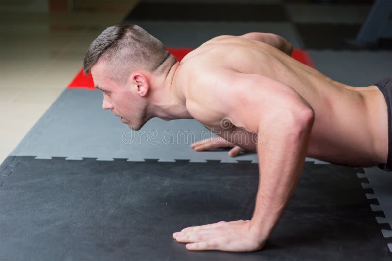 Man push up chest exercise and gritty serious facial expression inside gym.