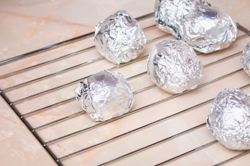 A Man Puts Raw Potatoes Wrapped in Foil on Wire Rack in the Oven. Stock