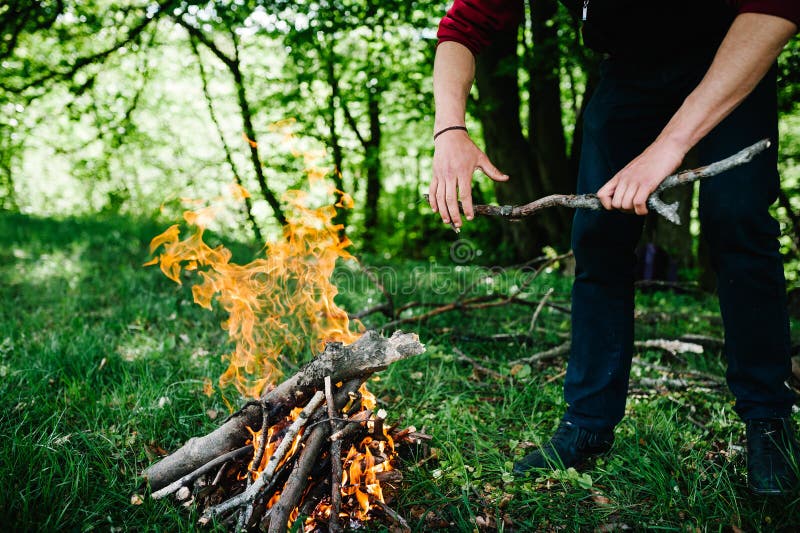 A man puts a stick in the fire, rest in the nature. The branch is in the hands of man