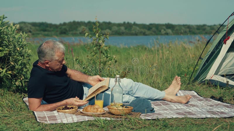 A man reads a book while relaxing in nature in the summer.