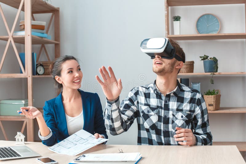 Young men at real estate agency sitting at table wearing virtual reality headset looking at new house project smiling joyful. Young men at real estate agency sitting at table wearing virtual reality headset looking at new house project smiling joyful