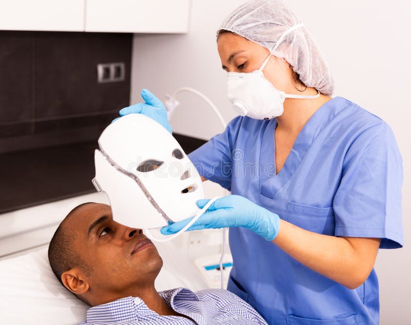 Man receiving facial light therapy in aesthetic medicine office