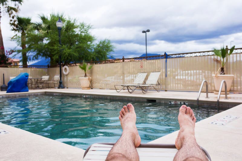 Legs of a man relaxing at the swimming pool in a yard. Legs of a man relaxing at the swimming pool in a yard