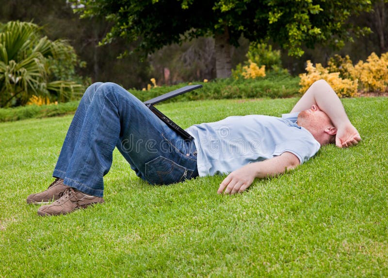 Man resting on lawn with half closed laptop