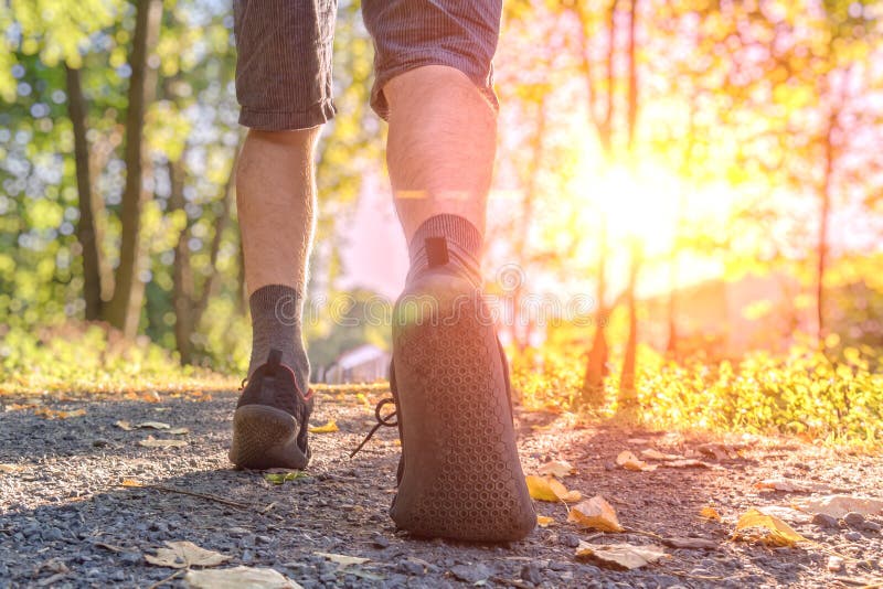 Man is running or walking at sunset. View on legs and feet from behind