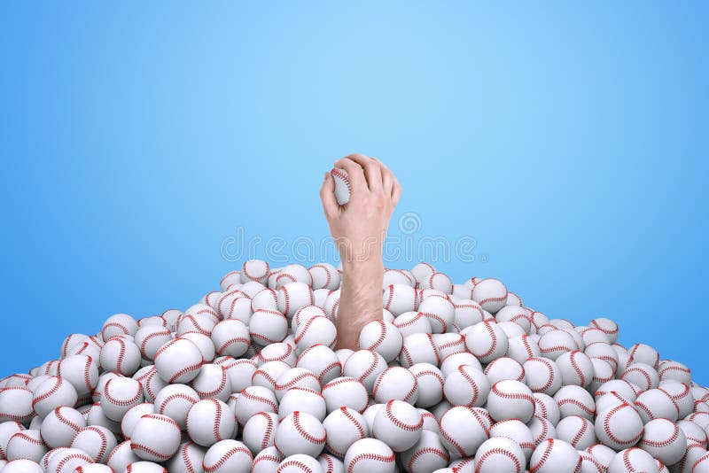 Man`s hand holding a baseball, emerging from under a big pile of baseballs. Sporting equipment. Snowed under in game. Popularity of sport grows,