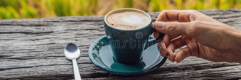 A man`s hand holds a cup of coffee on the background of an old wooden table BANNER, LONG FORMAT