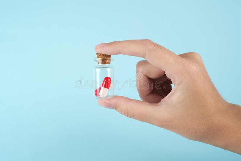 Man`s hand holds a glass transparent jar with pills on a light background close-up. medicines and vitamins. pharmaceuticals. chemical industry. remedies for viruses and bacteria. red and white pills