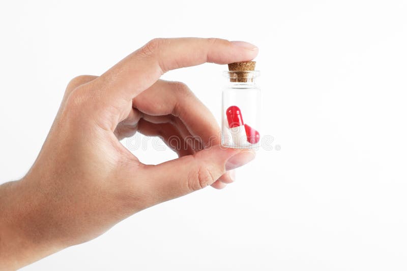 Man`s hand holds a glass transparent jar with pills on a light background close-up. medicines and vitamins. pharmaceuticals. chemical industry. remedies for viruses and bacteria. red and white pills