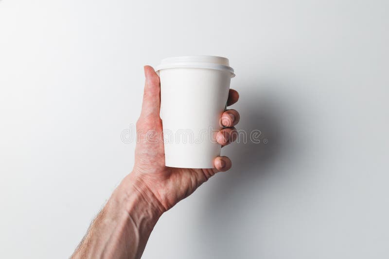 A man`s hand holds a paper coffee Cup on a white background. The concept of Breakfast and coffee. Take the drink with you.